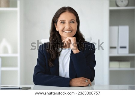 Jobs for older people, success in career in 40 plus age. Portrait of happy beautiful mature lady wearing formal suit posing at office, woman business consultant sitting at workdesk, smiling at camera Royalty-Free Stock Photo #2363008757