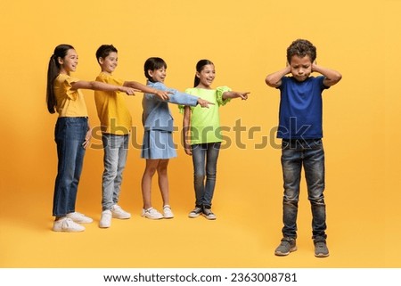 Bullying at school age concept. Multiracial laughing preteen kids pointing at upset boy, isolated on yellow background. Poor child suffering from mockery from his classmates, covering his ears Royalty-Free Stock Photo #2363008781
