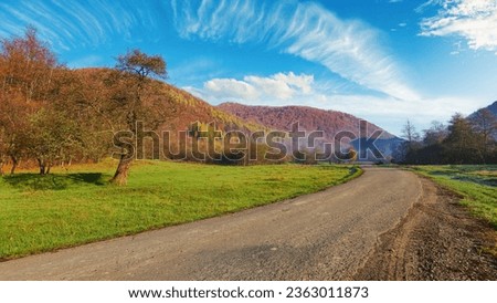 journey via road winding through countryside valley in autumn. forested hills in fall foliage. bright blue sky with white clouds