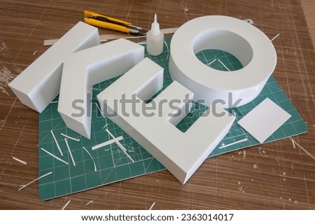 The white letters of the logo made of PVC plastic lie on the master's table.Production of outdoor advertising.Creating a company logo.