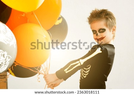 Halloween themed decorations. Boy in skeleton costume with makeup on his face with many balloons in orange and black for the celebration of All Saints Day.