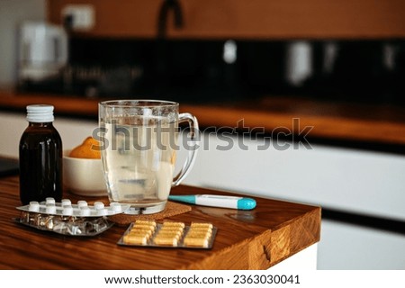 Natural and medical cold and flu remedies on table at home. Cold and flu influenza fall autumn and winter season. Cup with hot tea, lemon, thermometer pills and capsules Royalty-Free Stock Photo #2363030041