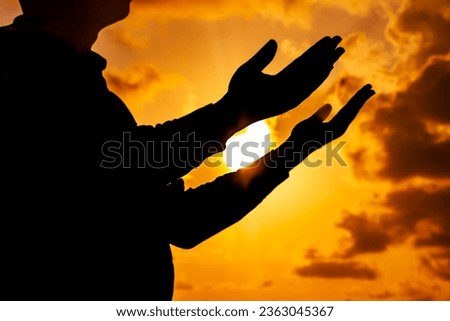 A breathtaking image of a lonely man, silhouetted against the vibrant colors of a sunset, deep in prayer during the solstice.