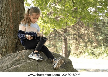 Little girl uses a tablet while sitting in the park in the summer