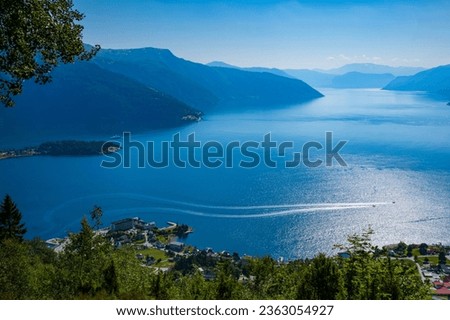 Two motorboats navigate the waters of Sognefjorden near the town of Balestrand, Norway during a summer afternoon where the blue sky and landscape merges. Photo taken from a mountain cliff on a hike.