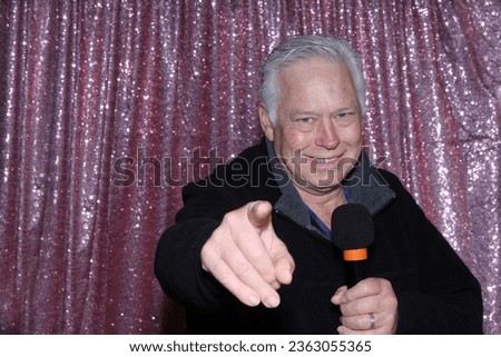 Lounge Singer. Photo Booth. A man with a Microphone Sings and Tells Jokes to entertain the crowd while he is in a Photo Booth waiting for his Pictures to be taken. Photo Booths are great for parties. 