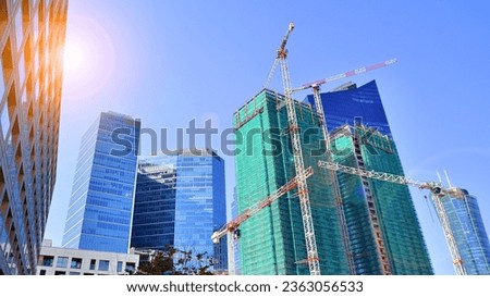 Modern high-rise buildings under construction next to glass skyscrapers in background. 