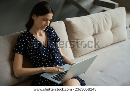 Female sits at home on couch and works on laptop Royalty-Free Stock Photo #2363058243