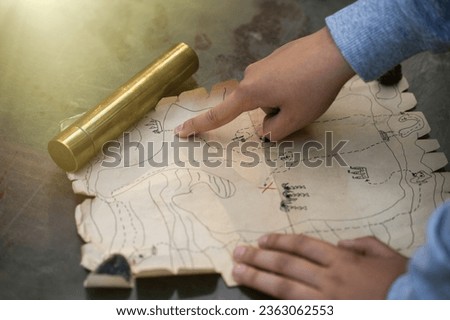 The child's hand points to the place of the buried pirate treasure on the map. A quest for children in the fresh air. A game of pirates. Children's holiday. Royalty-Free Stock Photo #2363062553