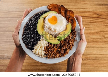 Woman's hands holding a typical Venezuelan food dish called pabellón criollo Royalty-Free Stock Photo #2363065341