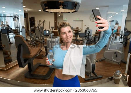 Attractive sports woman drinking water and making selfie on smartphone