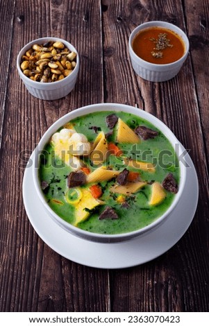 A bowl of Peruvian menestron soup. With chunks of meat, noodles, chopped carrots, corn and coriander to give it the green color.