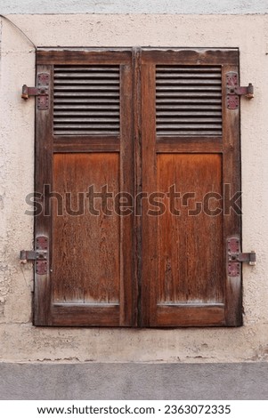 Country style window with closed ancient retro wooden shutters. Antique German historical house in Bavaria. Shabby cracked textured wall. Historic and atmospheric architect element. Front view
