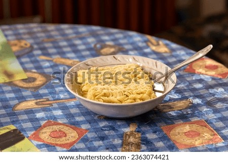 Instant noodles in a plate on the kitchen table, poured with boiling water. Junk food in the kitchen.