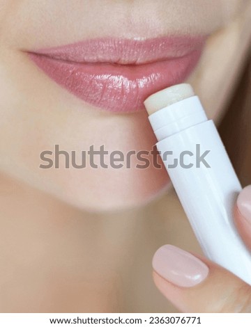 Lips skin protection. Close up portrait of beautiful woman holding a lipstick and applying hygienic balm. Natural make up Royalty-Free Stock Photo #2363076771