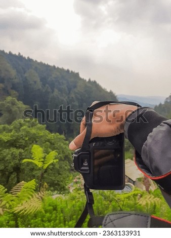 Hand holding the camera, landscape photography concept in the mountains. Kembanglangit park or Forest Kopi kembang Langit