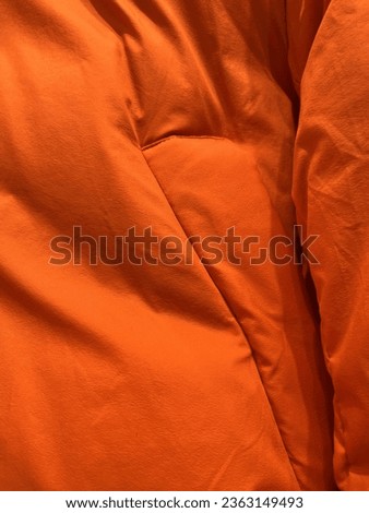 Close up orange colored clothing fabric with visible folds texture for fashion themed industry photography.