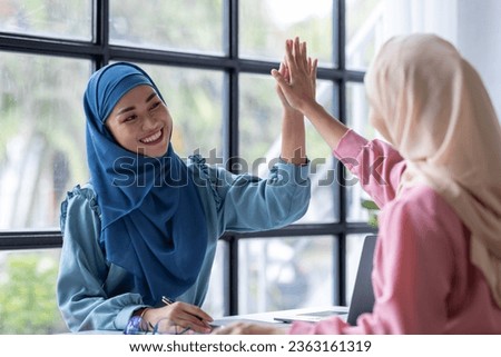 Young two beautiful smiling happy excited asian muslim women relaxing using laptop computer working and meeting analyzing discussing strategy with startup project plan and brainstorm in office