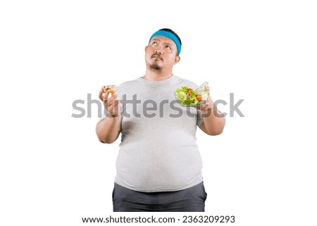 Overweight asian guy choosing between healthy and unhealthy food - vegetables salad or doughnut