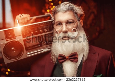 A modern Santa Claus in an elegant three-piece suit dances and laughs with a tape recorder in his hands in a magical Christmas setting. Fun fashionable party for Christmas and New Year. 
