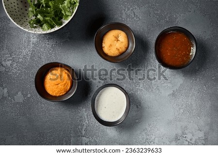 A top view shot displaying a variety of sauces in individual bowls, gracefully laid out on a gray backdrop. The minimalist composition accentuates the vivid colors and textures of each sauce.