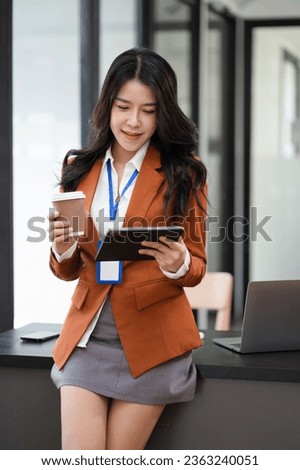 Happy young woman looking at tablet screen, reading message, or email, communicating distantly with client  work in modern office.