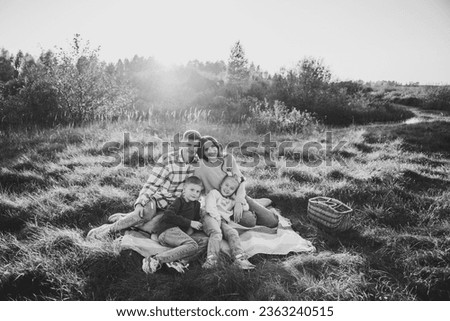 Happy family walking spending time together in nature. Mom, dad, daughter, son sits on blanket, hugs in grass in field at sunset. Family holiday outdoors. Kids embrace parents. Black and white photo