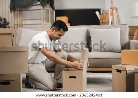 Young man carrying packed cardboard boxes with personal belongings to unfurnished cozy living room during move-in relocation day to new apartment. 