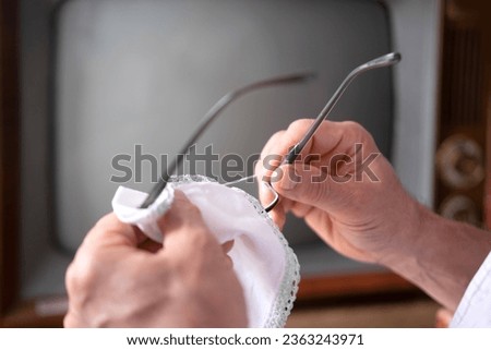 male hands cleaning reading glasses to watch Old-Fashioned retro analog TV 1960-1970, stylish Retro Technology in Everyday Life Royalty-Free Stock Photo #2363243971