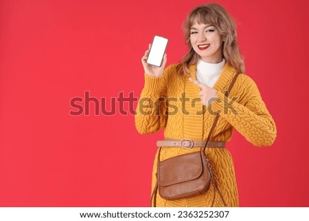 Stylish young woman pointing at mobile phone on red background