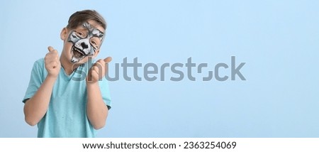 Funny little boy with face painting showing thumb-up on light blue background with space for text Royalty-Free Stock Photo #2363254069