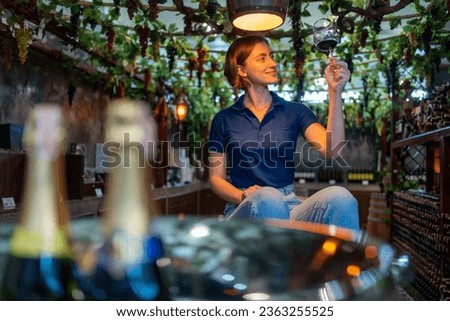 Professional Caucasian woman sommelier tasting and smelling red wine in wine glass at wine cellar with wooden barrel at wine factory. Alcohol liquor shop, winery industry and winemaker concept. Royalty-Free Stock Photo #2363255525