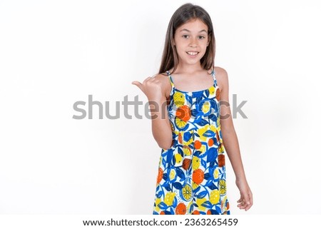 Lovely Beautiful kid girl wearing flowered dress over white background pointing aside with forefinger, showing at copy space having news about bargains