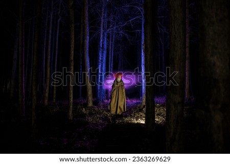 a scary evil clown wearing a dirty costume in the woods at night. Night forest, horror Halloween concept