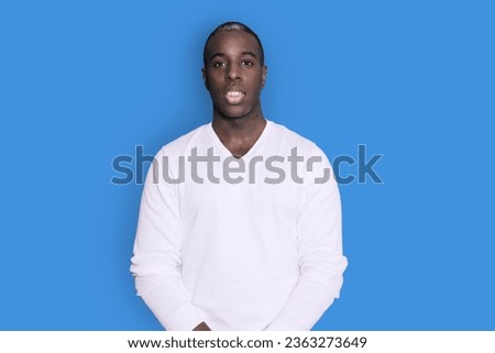 Portrait of cheerful young african-american guy wearing white casual sweater posing isolated on blue background. Carefree young millennial man looking at camera and laughing