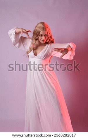 Close up portrait of beautiful blonde model wearing elegant  white halloween gown. arms reaching out like hungry vampire.  isolated on studio background with  red cinematic moody lighting.