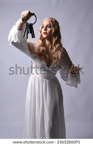 Close up portrait of beautiful blonde model wearing elegant  white halloween gown, a historical fantasy character. Holding old key chain, isolated on studio background.