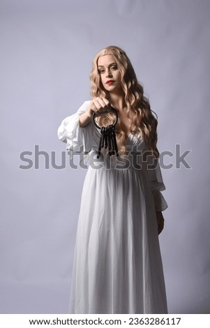 Close up portrait of beautiful blonde model wearing elegant  white halloween gown, a historical fantasy character. Holding old key chain, isolated on studio background.