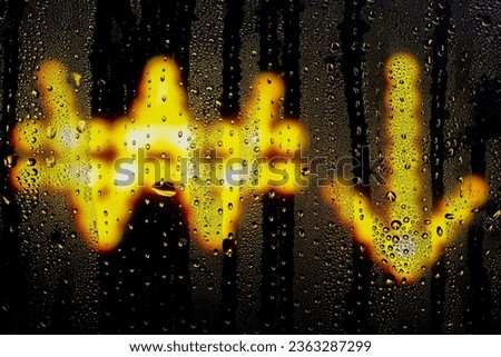 Blurred glowing Korean won sign with arrow down made from light bulbs.The symbol of the national currency behind a rain-wet window with water drops in the night.Sign of economic crisis.
