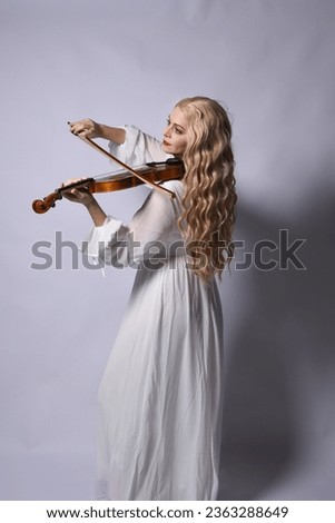 Close up portrait of beautiful blonde model wearing elegant  white halloween gown, a historical fantasy character.  Holding a violin musical instrument, isolated on studio background.