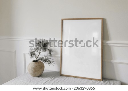Minimal Christmas Scandinavian interior. Winter seasonal art display. Side view of blank vertical wooden picture frame, poster mockup. Pine tree branches in old vase on table. White wall background