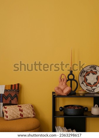 Cozy living room interior with yellow wall, stylish bench, patterned pillows, candle with candlestick, black rack, sculpture, books, colorful baskets and personal accessories. Home decor. Template.