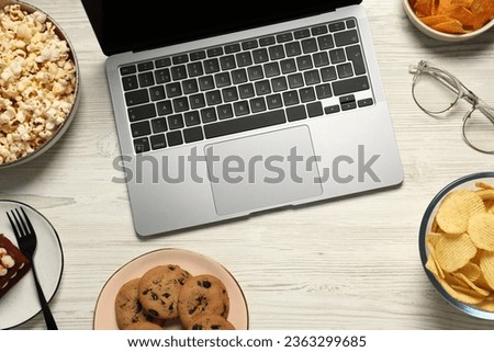 Bad eating habits at workplace. Laptop, glasses and different snacks on white wooden table, flat lay