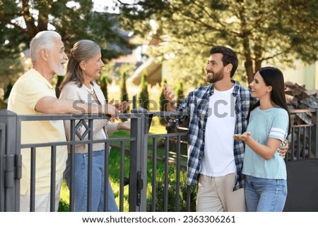 Friendly relationship with neighbours. Young family talking to elderly couple near fence outdoors Royalty-Free Stock Photo #2363306261