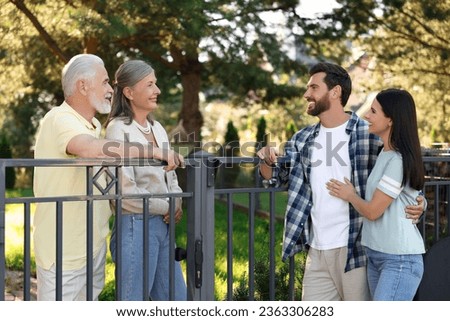 Friendly relationship with neighbours. Young family talking to elderly couple near fence outdoors Royalty-Free Stock Photo #2363306283