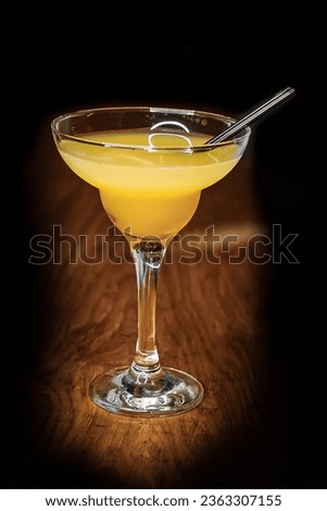 Cocktail alcoholic glass with orange juice and a straw stands on the bar counter on a dark background vignette.