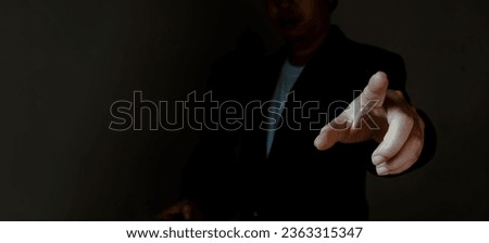 A stylish gentleman donning a sleek suit in a dimly lit room, employing expressive hand gestures illuminated with striking clarity to convey various symbolic messages.