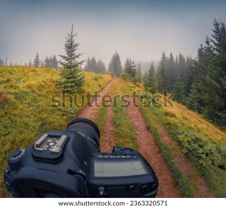 Digital camera on a tripod takes pictures of old country road. Foggy autumn scene of Carpathian mountains, Krasnyk village location, Ukraine, Europe. Beauty of countryside concept background.
