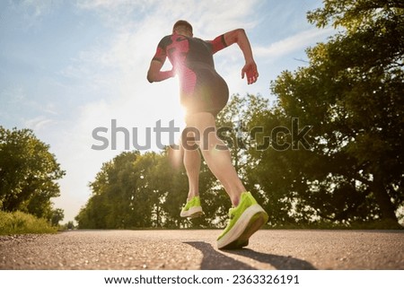 Back view dynamic image of sportsman, runner in sportswear training, running alone the road. Concept of professional sport, triathlon preparation, competition, athleticism Royalty-Free Stock Photo #2363326191