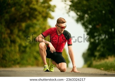 Feeling tired. Sportsman in sportswear standing on one knee after hard training run and resting. Concept of professional sport, triathlon preparation, competition, athleticism
